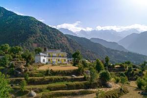 a house on a hill with mountains in the background at The Hosteller Kareri in Dharamshala