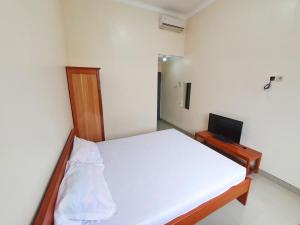 a small bedroom with a white bed and a television at Griya Shinta Syariah Solo Mitra RedDoorz in Bonorejo