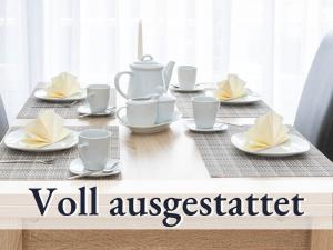 una mesa con tazas blancas y platillos en ella en Große moderne Ferienwohnung in bester Bodenseelage l 1 Minute zum Bodensee l 2 Zimmer l Vollausgestattete Küche l Sonnenbalkon l WLAN l Willkommen im Apartment Güttingen, en Radolfzell am Bodensee