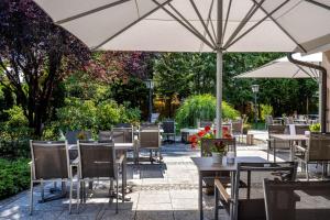 ein Restaurant im Freien mit Tischen, Stühlen und einem Sonnenschirm in der Unterkunft Best Western Plus Hotel Erb in Parsdorf