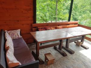 une table en bois et un canapé sur une terrasse couverte dans l'établissement Potok kuca sa bazenom, à Konjic