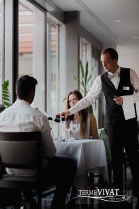 a man in a tuxedo waiter serving people at a table at Hotel Vivat in Moravske Toplice