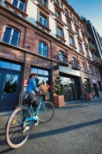a woman riding a bike in front of a building at Hôtel Tandem - Boutique Hôtel in Strasbourg