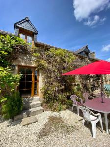 a table with a red umbrella in front of a building at Gîtes Les Villes Briend in Pluduno