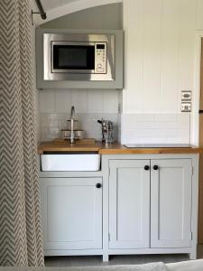 a kitchen with white cabinets and a microwave at Self-catering shepherds hut with private garden in Durhams idyllic countryside in Durham