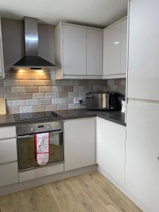uma cozinha com armários brancos e um forno com placa de fogão em Chase Bungalow em Billericay
