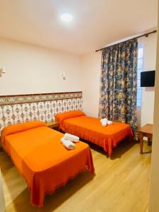 two beds in a room with orange sheets at HOSTAL LA CAÑADA RUIDERA in Ossa de Montiel