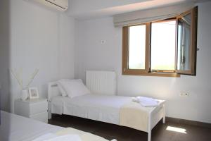 een witte slaapkamer met een bed en een raam bij Villeta Nikol “Νηνεμία” in Lixouri