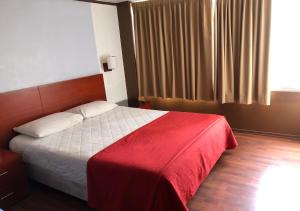 a bedroom with a bed with a red blanket and a window at Filatelia Suites & Travel in Quito