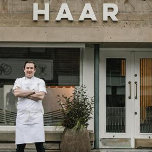 a man standing in front of a building with his arms crossed at Haar with Rooms 5 stars in St Andrews