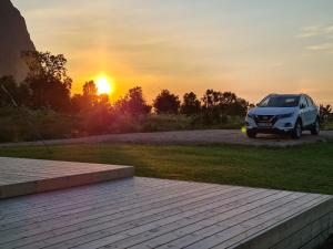 un coche blanco estacionado en un campo con la puesta de sol en Lauvåsstua-Charming house by the sea en Bøstad