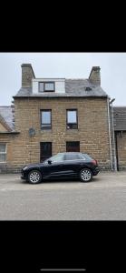 a black car parked in front of a brick building at NC500, Wick Caithness Holiday Home in Wick