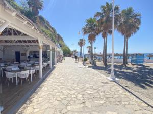 chodnik ze stołami, krzesłami i palmami na plaży w obiekcie Azahara En Suite Casasol w mieście Nerja
