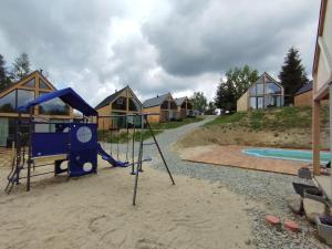 a playground with a slide in the sand and some houses at Stodoły Hołosanka 600-065-145 in Polańczyk