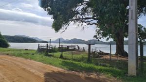 a dirt road next to a lake with a fence at Hostel Lagoa do Sol in Saquarema