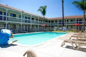 a swimming pool in front of a hotel with chairs and palm trees at Motel 6-Carlsbad, CA Beach in Carlsbad