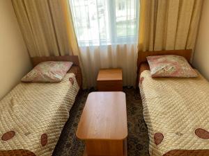 two beds in a room with a table and a window at Guest house Aidyn-Kul in Toguz-Bulak