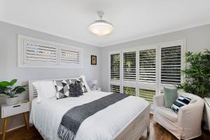 a white bedroom with a bed and a chair and windows at Sandcastles in Budgewoi