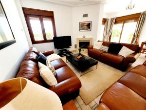 ein Wohnzimmer mit Ledersofas und einem TV in der Unterkunft Villa Jacaranda Altaona Golf in Murcia