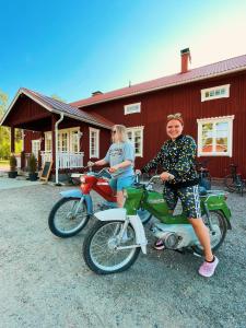 une femme est assise sur une moto devant une maison rouge dans l'établissement Tackork Gård & Marina, à Nauvo