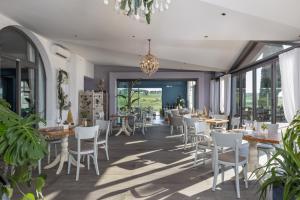 um restaurante com cadeiras brancas, mesas e janelas em Golf Club Bellosguardo resort em Vinci