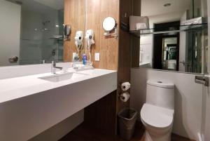 a bathroom with a sink and a toilet and a mirror at Ramada Encore by Wyndham Guadalajara Aeropuerto in Guadalajara