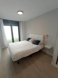 a white bed in a room with a large window at Apartamento LA ESTACIÓN con terraza in Gijón