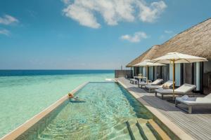 una piscina sulla spiaggia con sedie e ombrelloni di COMO Maalifushi - Partner Travels FREE for 7 Nights or More a Maalifushi