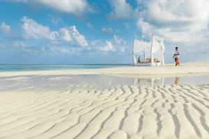 a person standing on a beach with a sail boat at COMO Maalifushi - Partner Travels FREE for 7 Nights or More in Maalifushi