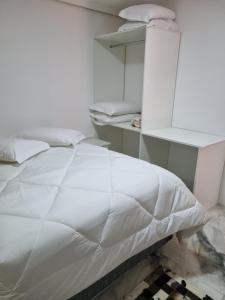 uma cama branca num quarto com uma prateleira em Casa elmar em Canela