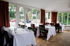 un restaurante con mesas y sillas blancas y ventanas en Riverdale Hall Hotel & Leisure, en Bellingham