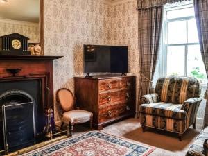 un salon avec une télévision, une chaise et une cheminée dans l'établissement Beautiful Traditional secluded country cottage, à Sanquhar
