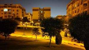 a park with trees and buildings at night at Lovely 2-bedrooms Apartment with free parking in Madīnat ash Shurūq