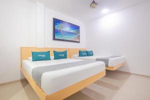 two beds in a white room with blue pillows at Ayenda Alameda Real in Montería
