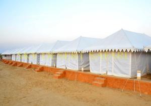 a row of white tents in a field at Sky Desert Safari Camp Jaisalmer in Jaisalmer
