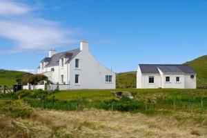 una casa blanca en una colina con un campo de hierba en 7B Ardroil, en Uig