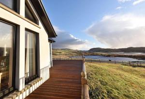a house with a wooden deck next to the water at Ceann an Loch Cottage in Balallan