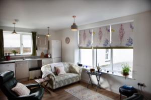 un salon avec un canapé et une chaise et deux fenêtres dans l'établissement Ceannard Cottage, à Howmore