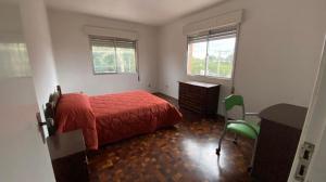 a bedroom with a red bed and a desk and two windows at Apartamento com dois quartos no fragata in Pelotas
