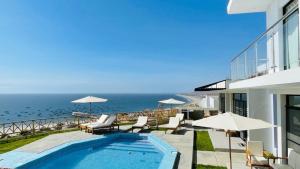 ein Swimmingpool mit Liegen und Sonnenschirmen und das Meer in der Unterkunft VISTA LINDA BUNGALOW para 4 personas Punta Veleros in Los Órganos