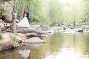 a bride and groom standing on rocks next to a river at The Don Hoel Resort & Venue in Sedona