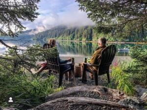 2 personnes assises sur des chaises en face d'un lac dans l'établissement Between Beaches Alaska, à Seldovia