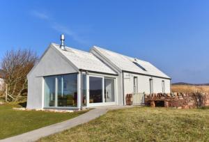 a small white house with large windows on a field at Taigh Glas in Gairloch