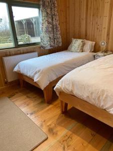 two beds in a room with wooden floors and a window at Rural Wood Cabin - less than 3 miles from St Ives in Penzance
