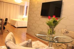 a living room with a tv and a glass table with roses at Hotel Areias Brancas in Rosário do Sul