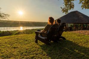 deux personnes assises sur un banc et regardant le coucher du soleil dans l'établissement Crocodile Bridge Safari Lodge, à Komatipoort