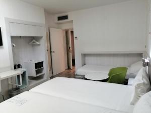 a white bedroom with a bed and a green chair at Ibis Styles Madrid Prado in Madrid