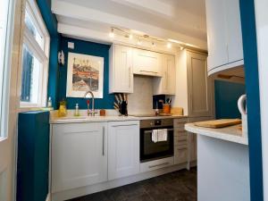 una cocina con armarios blancos y una pared azul en Pass the Keys 3 Bed Terrace with fantastic views over estuary, en Aberdyfi