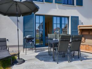um pátio com uma mesa, cadeiras e um guarda-sol em Reetland am Meer - Luxus Reetdachvilla mit 3 Schlafzimmern, Sauna und Kamin F15 em Dranske