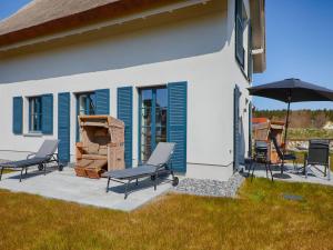 a patio with chairs and an umbrella next to a house at Reetland am Meer - Superior Reetdachvilla mit 2 Schlafzimmern, Kamin und 2 Terrassen F17 in Dranske